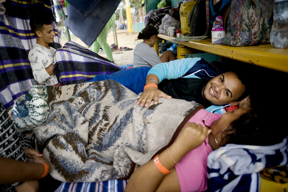 Tomas Torres puts his hand on the stomach of his pregnant wife, Elvia Perez de Torres, as they rest at a camp for migrants at a sports facility in Tijuana, Mexico. (CNS/David Maung)