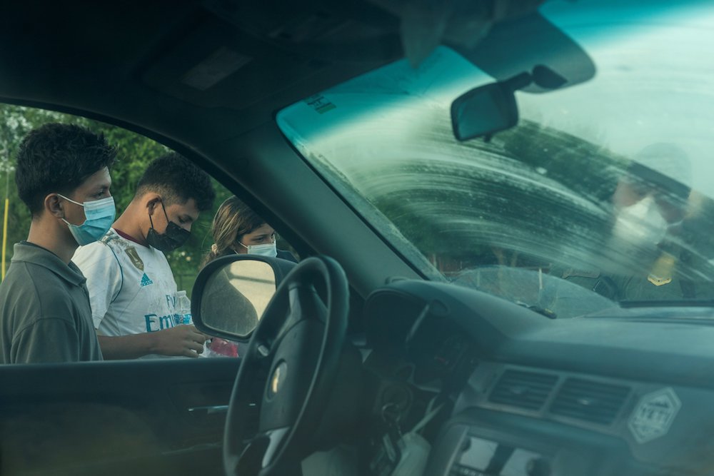 Migrants from Central America in Penitas, Texas, are seen next to a car as they are processed by a U.S. Border Patrol agent after crossing the Rio Grande July 8. (CNS photo/Go Nakamura, Reuters)