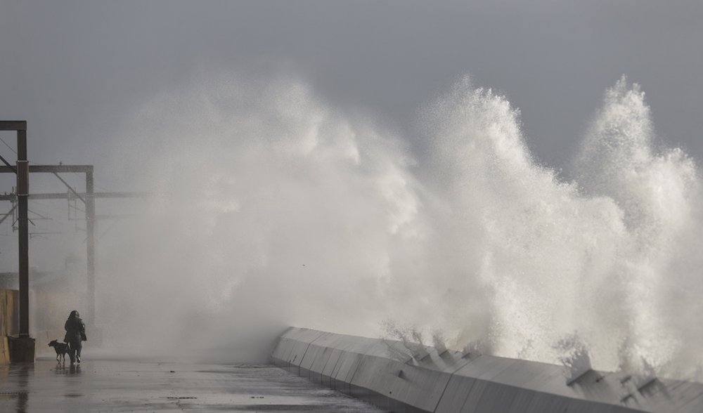 A man walks his dog in February 2020 as waves crash against a seawall in Saltcoats, in Scotland, the country where the U.N. climate conference is scheduled to end Nov. 12. (CNS photo/Eddie Keogh, Reuters)