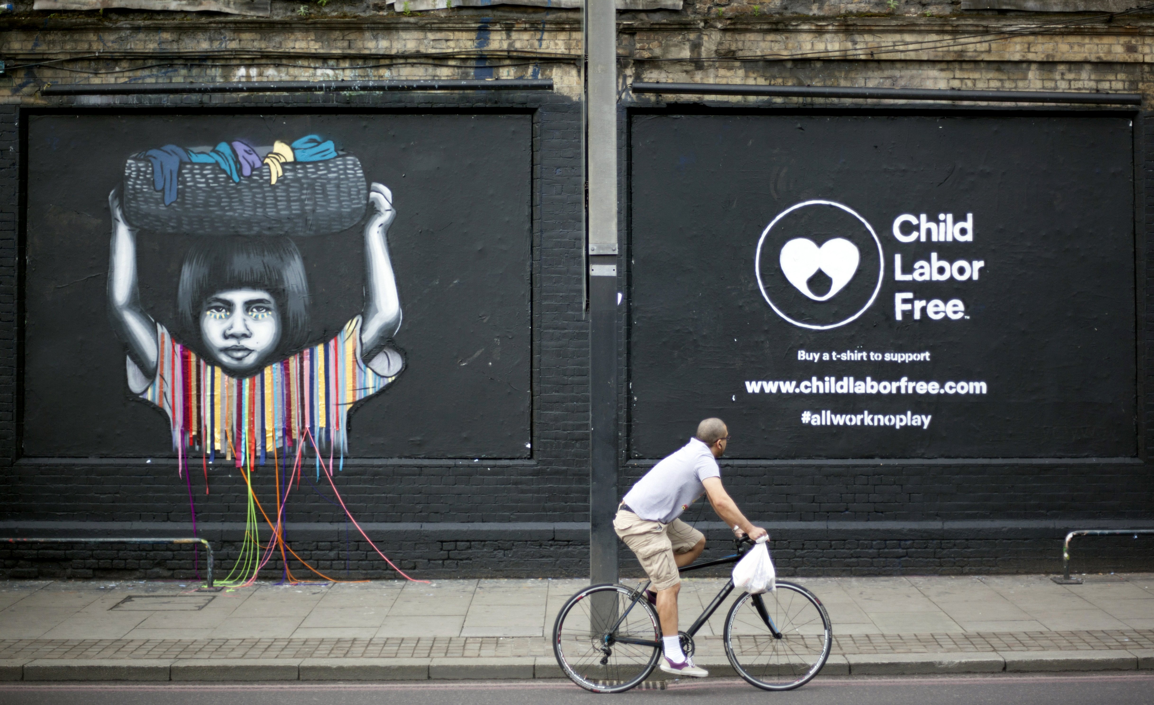 A cyclist passes a mural created by street artists depicting child labor in London June 8, 2016. (CNS photo/Shanshan Chen, Reuters)