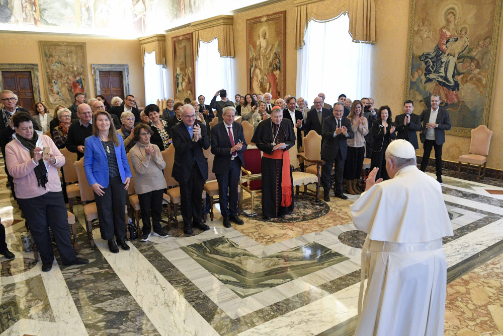 Pope Francis stands in front of a large group of people in the Vatican