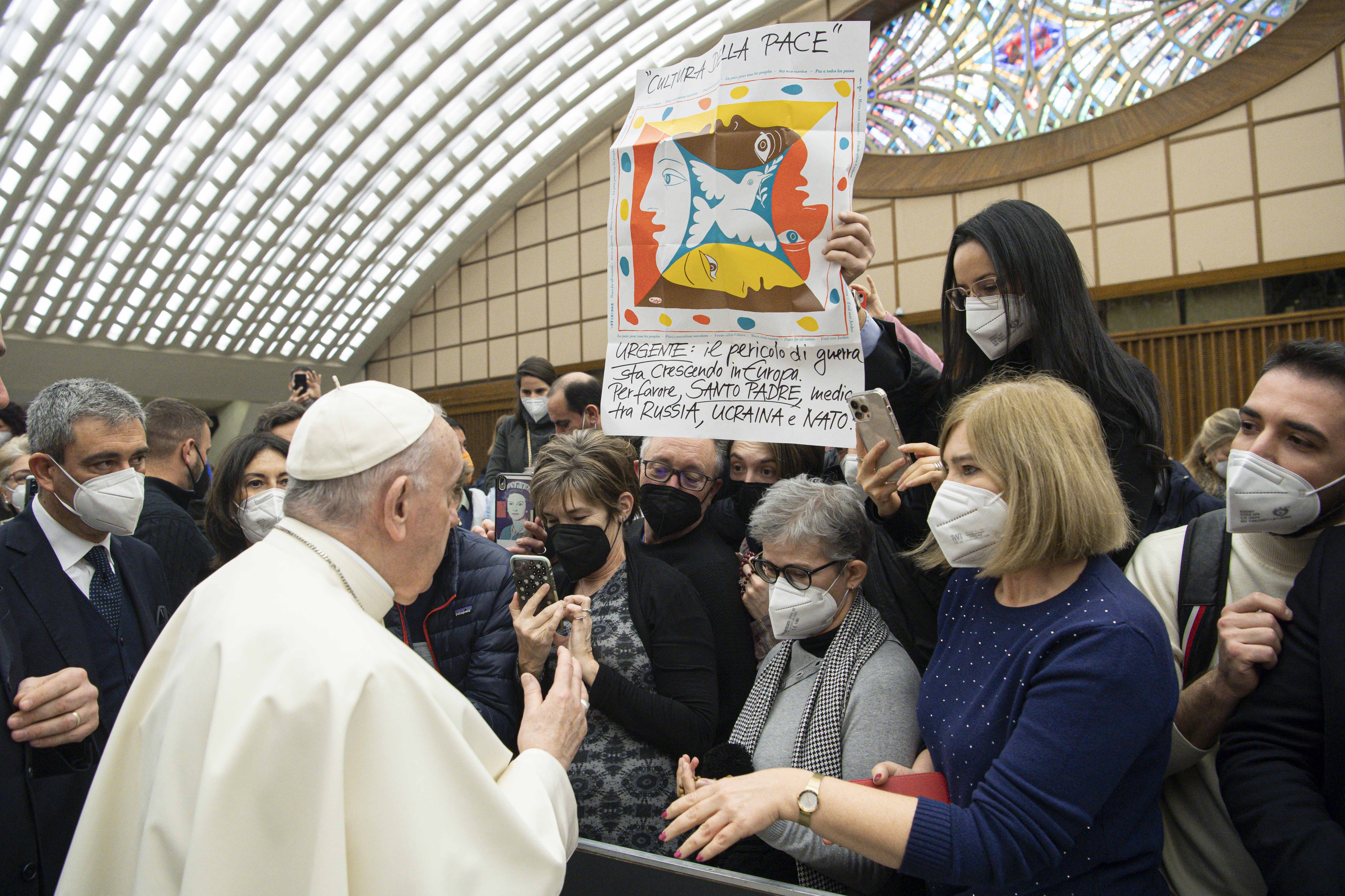 Pope Francis greets people near a banner in Italian calling for the pope's intervention with Russia, Ukraine and NATO, during his general audience in the Paul VI hall at the Vatican Jan. 19, 2022. (CNS photo/Vatican Media)