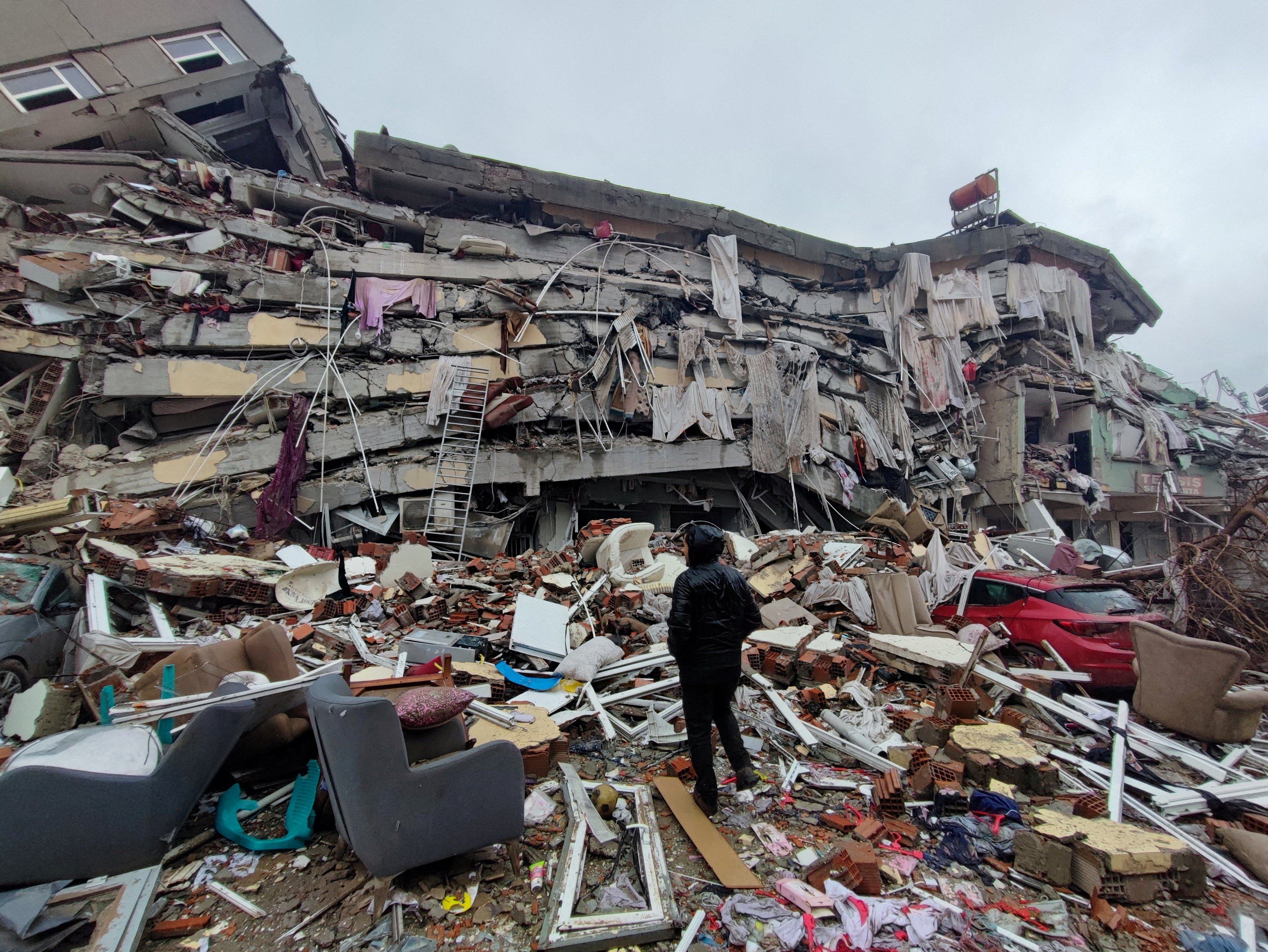 A person stands in front of a massive collapsed building