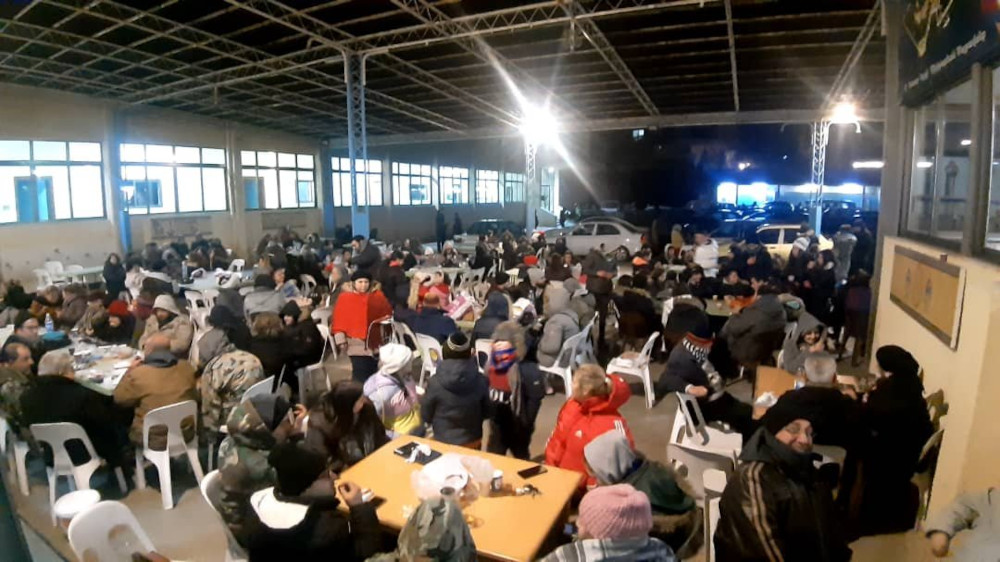 Many people in winter clothing gather at tables in a warehouse-looking space