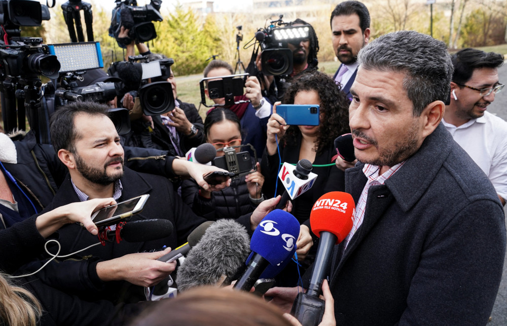 People with microphones and professional cameras crowd around a brown man