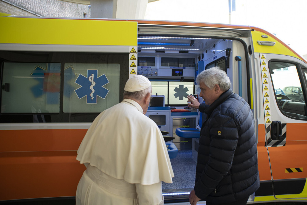 Pope Francis stands outside an ambulance with an older white man in a puffy jacket