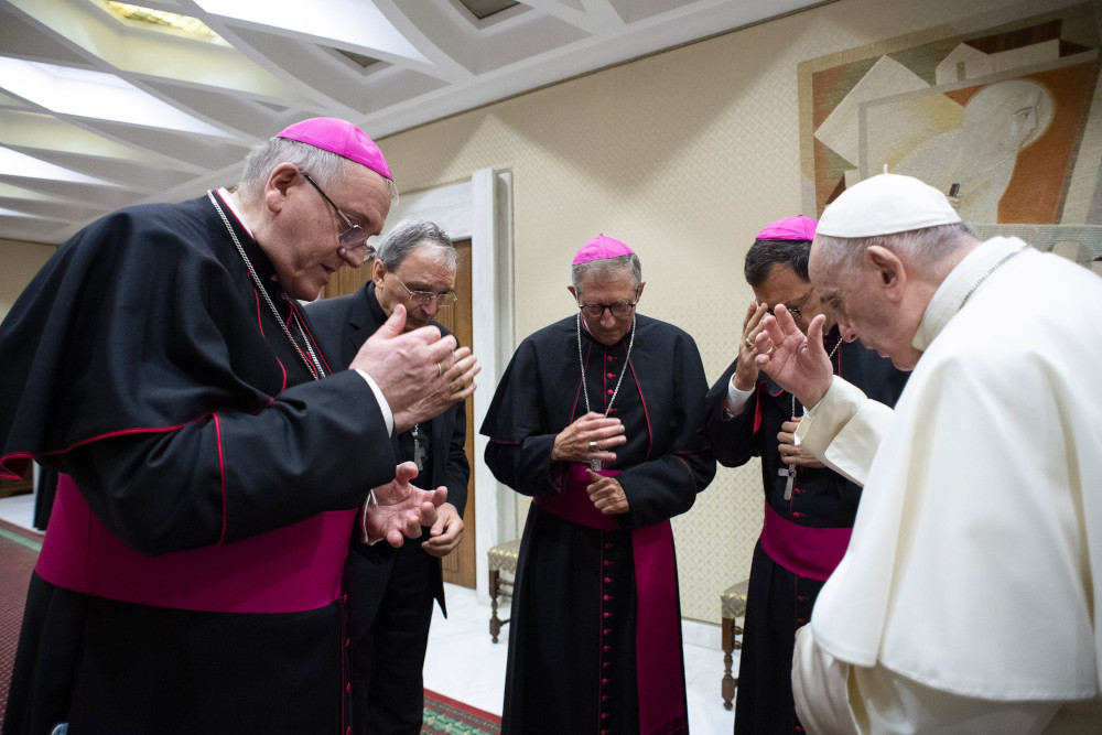 Pope Francis and four bishops stand in a circle with bowed heads as they make the sign of the cross