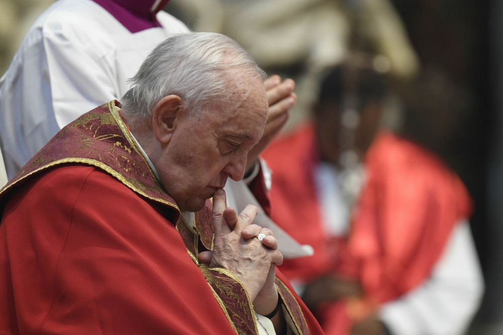 Pope Francis, dressed in red and gold and without a zucchetto, bends his head in prayer