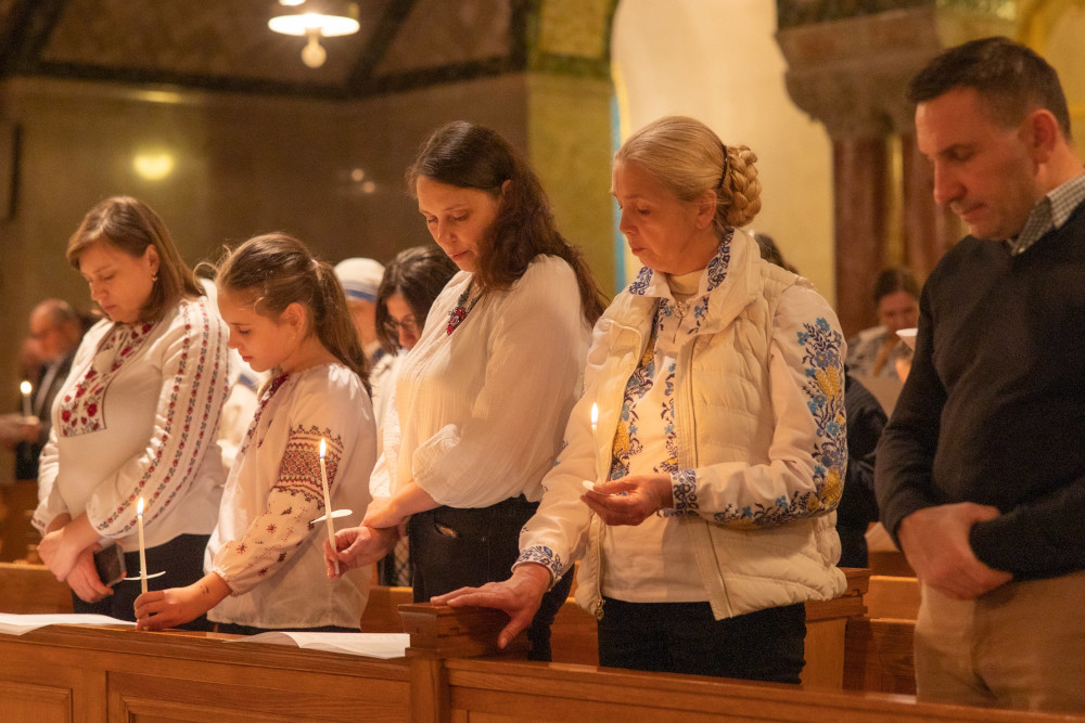 Five people, some wearing brightly embroidered sweaters and shirts, hold candles