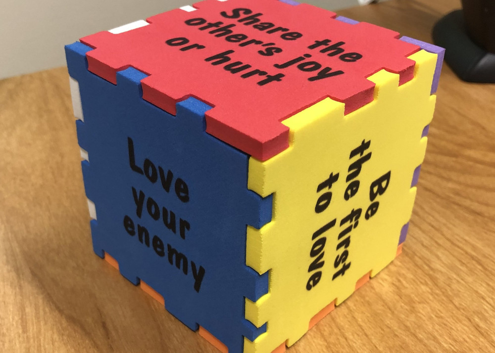 A cube in primary colors has phrases like, "Be the first to love," "Share the other's joy or hurt," and "Love your enemy."