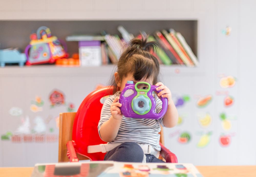 Little girl with toy camera covering her face