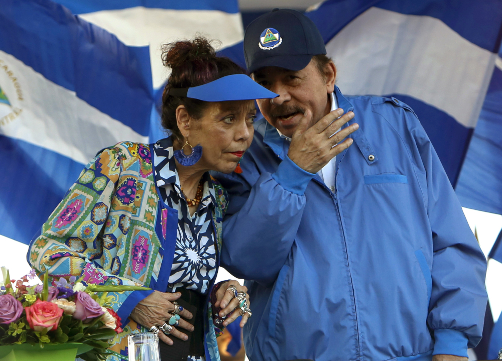 A man wearing a light blue coat talks into the ear of a woman wearing a similar colored visor