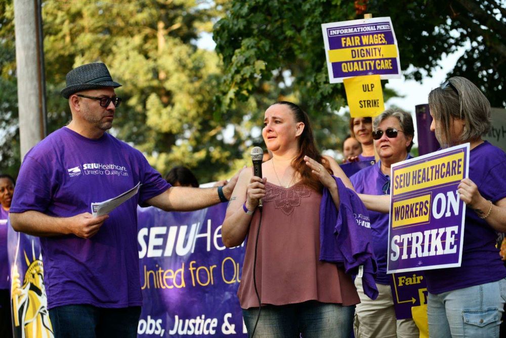 Woman holds microphone while others near her hold signs supporting the union.