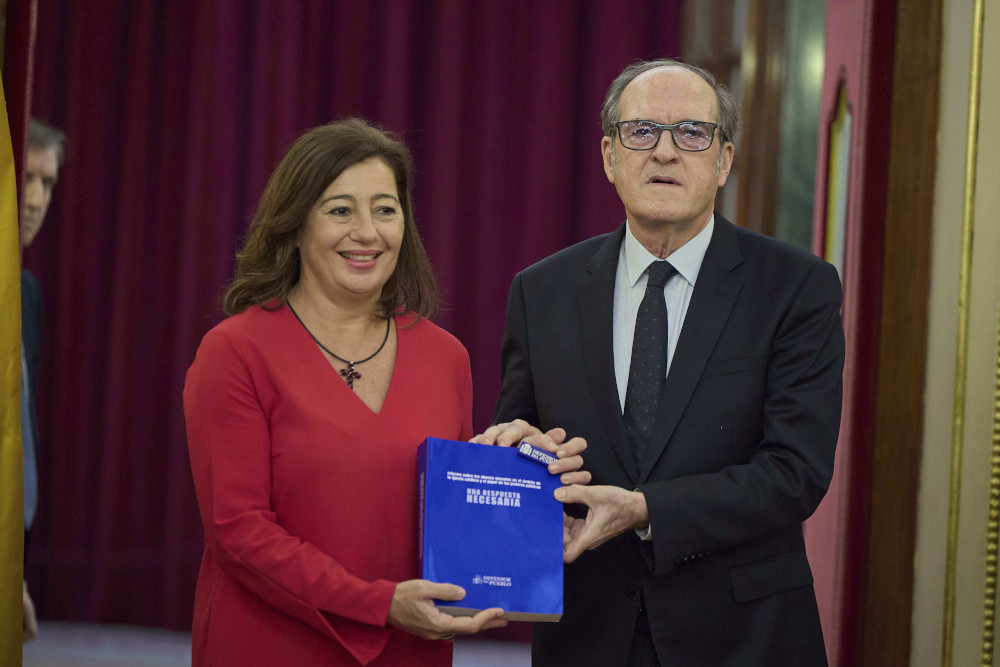 A woman and a man in Western business attire stand next to each other holding a blue book