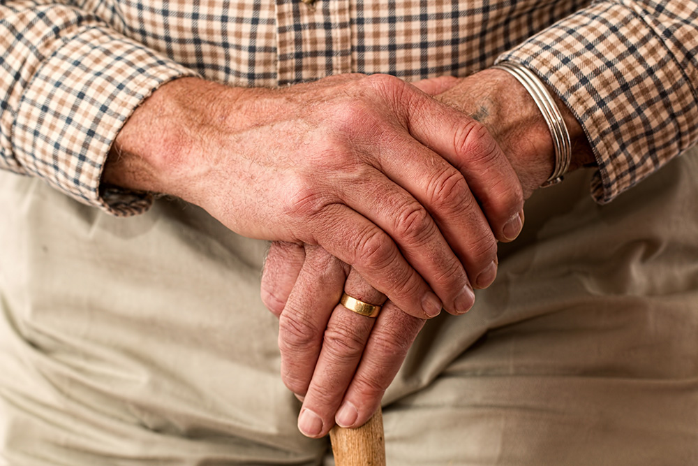 An elderly man's hands, wearing a wedding ring, rest on a cane (Pixabay/Steve Buissinne)