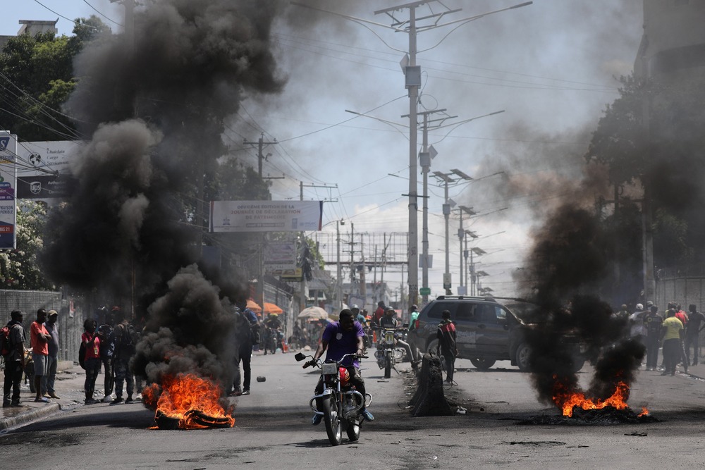 Motorists pass a burning barricade in Port-au-Prince