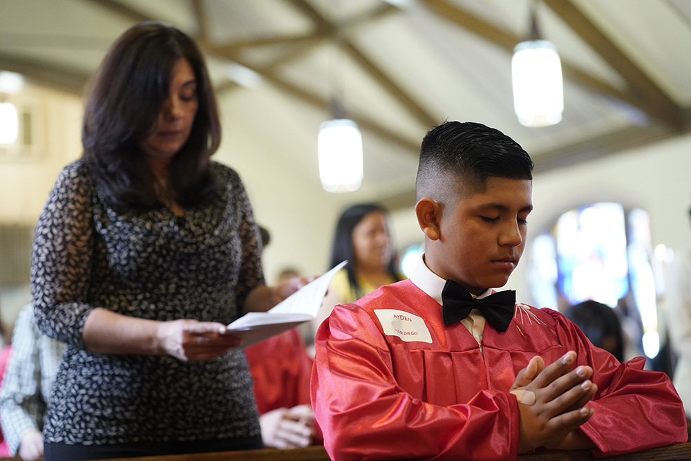 Confirmation candidate Ayden Morocho kneels in prayer as his sponsor, Grace Esposito, stands behind him during a confirmation Mass on May 5, 2022, at Holy Family Church in Queens, New York. (CNS/Gregory A. Shemitz)