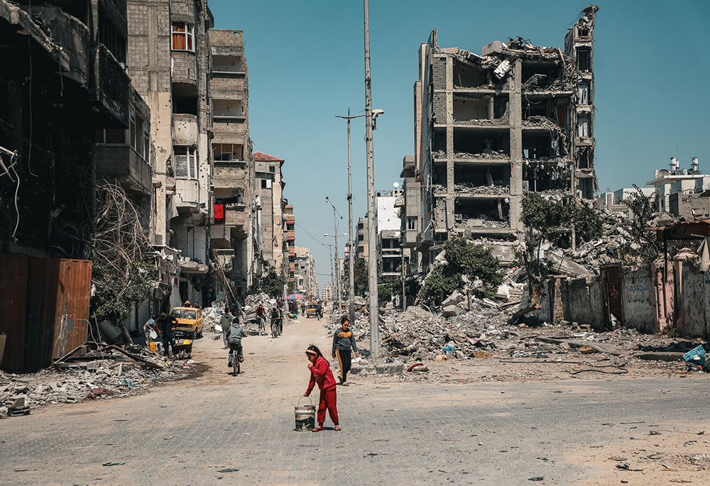 A child carries a bucket along a row of destroyed buildings March 16 in Gaza City. (OSV News/Courtesy of Caritas Poland)