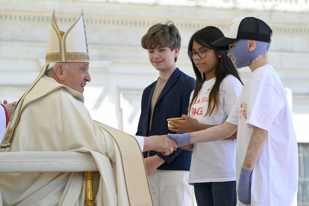 Pope Francis, vested, sits as he receives children. 