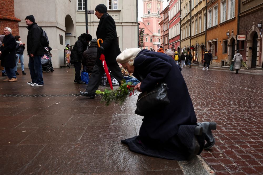 A woman kneels in front of the cathedral in Warsaw, Poland, on the anniversary of St. John Paul II's death April 2, 2023. 