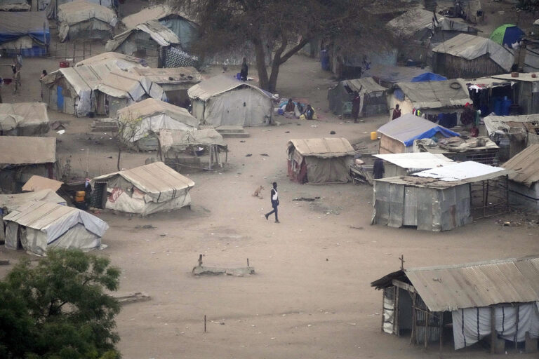 Person walks through large, dusty square enclosed by shanties. 
