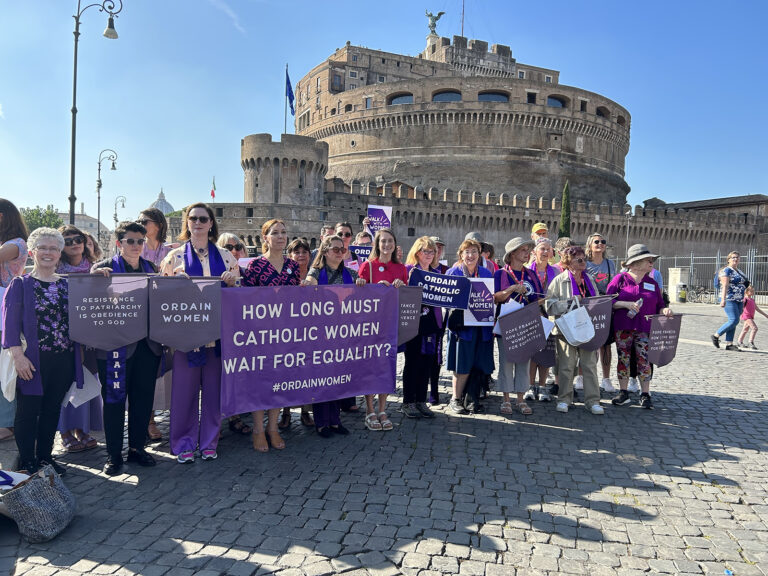 Women hold banners, in background is the Castel Sant'Angelo