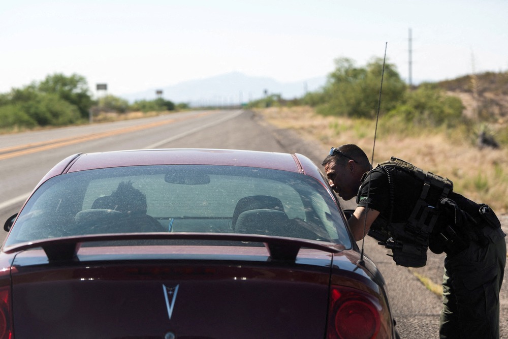 Officer leans into passenger window of red car on long desert road