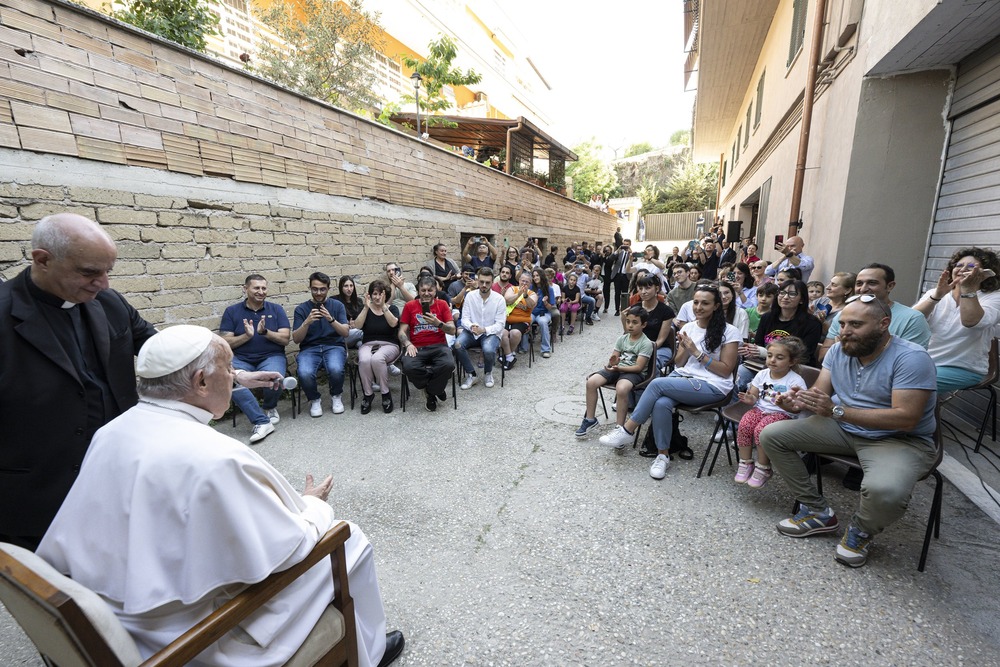 Pope Francis, seated, pictured from behind facing apartment residents in brick courtyard