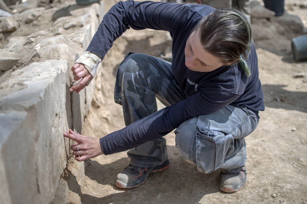 Archaeologist kneels down to examine stone structure