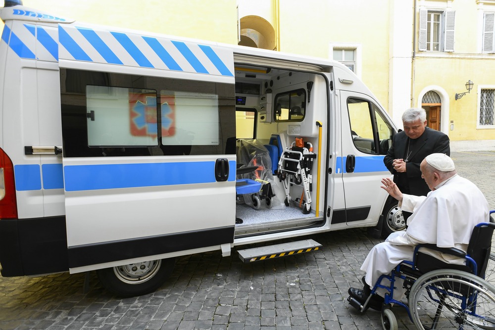 Pope Francis, in wheel chair, raises hand in blessing over ambulance