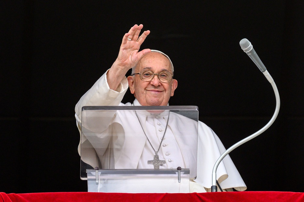 Pope Francis, smiling, waves from St. Peter's Square balcony