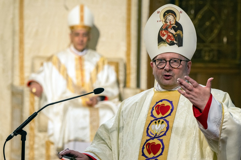 Bishop Waller, vested, speaks at lectern, while Cardinal Fernandez, also vested, sits ex cathedra. 
