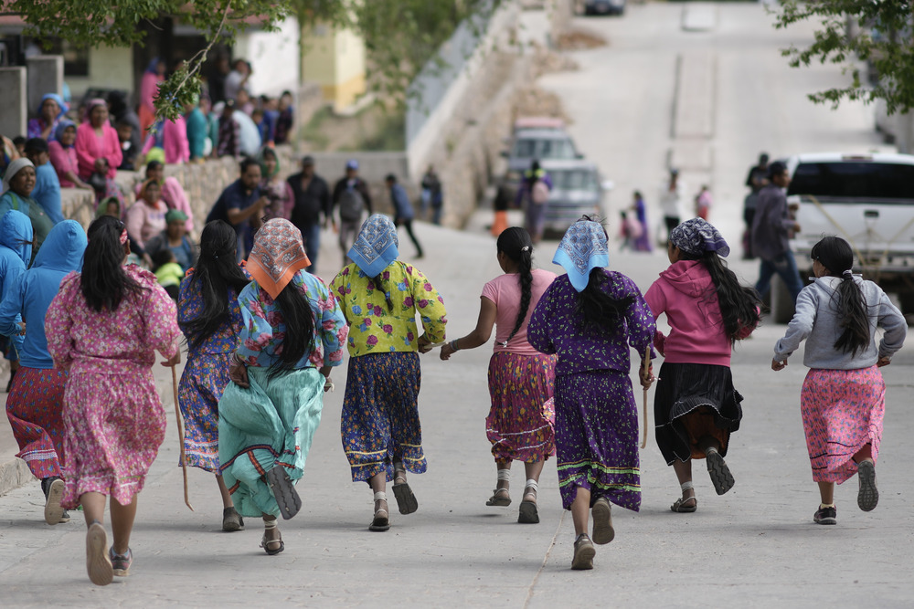 Women wearing brightly colored skirts and headscarves, pictures from behind, running through street.
