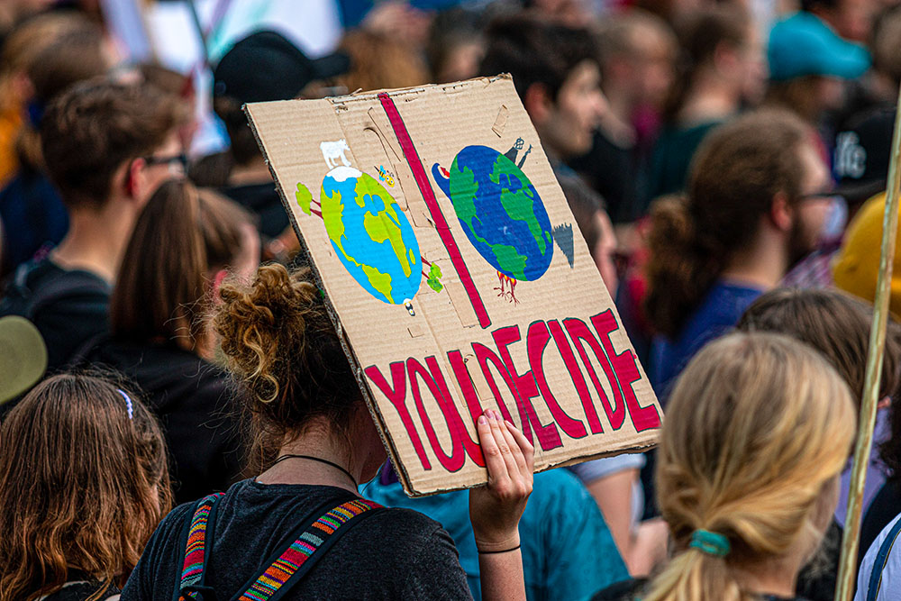 Protester holds a sign with painted images of two Earths and the words "YOU DECIDE" (Pixabay/dmncwndrich)