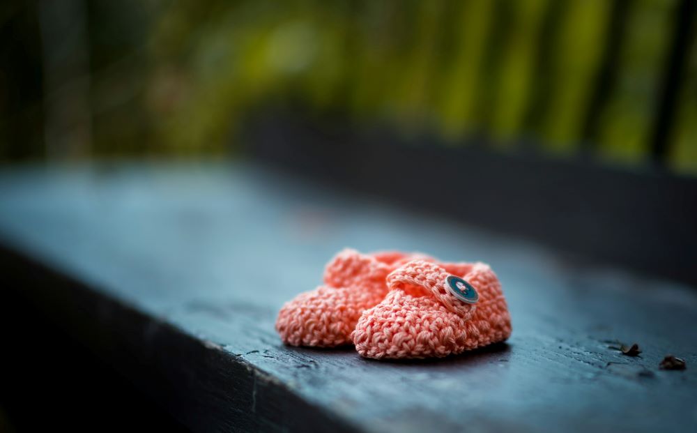 pink knitted baby shoes on a bench (Unsplash/🇸🇮 Janko Ferlič)