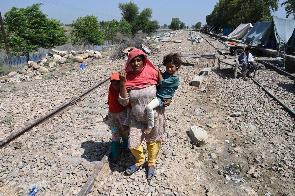 A pregnant flood-affected woman carries her child as she walks near her tent at a makeshift camp along a railway track in India’s Punjab province in September 2022. (Grist/AFP via Getty Images/Arif Ali)