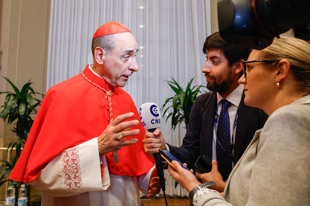 Fernandez wears red Cardinal's clerics and speaks to reporters. 