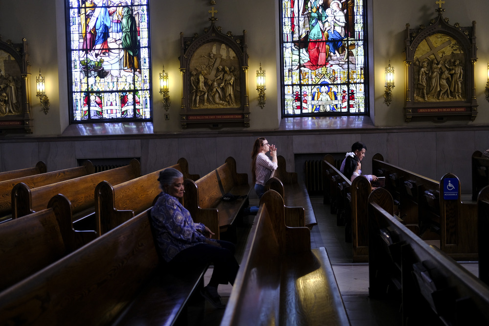 Stained glass windows, stations of the cross, and people kneeling. 