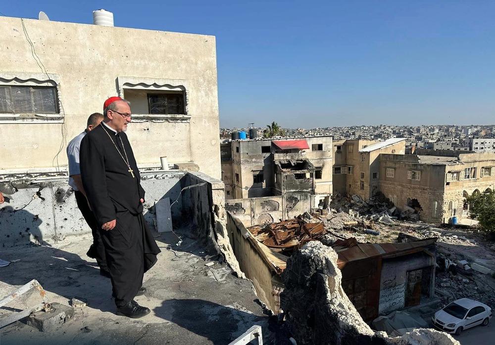 Pizzaballa stands on rooftop surveying vast ruins; the cardinal wears plain black clericals, with a red zucchetto.