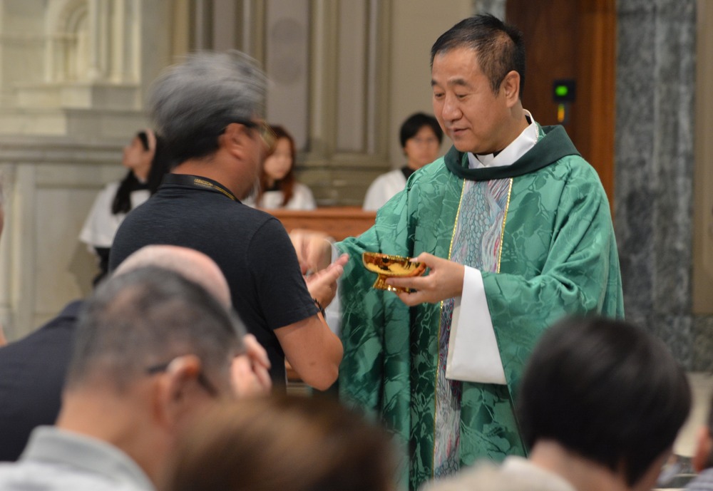 Pei, vested in green, hands Eucharistic host to person. 