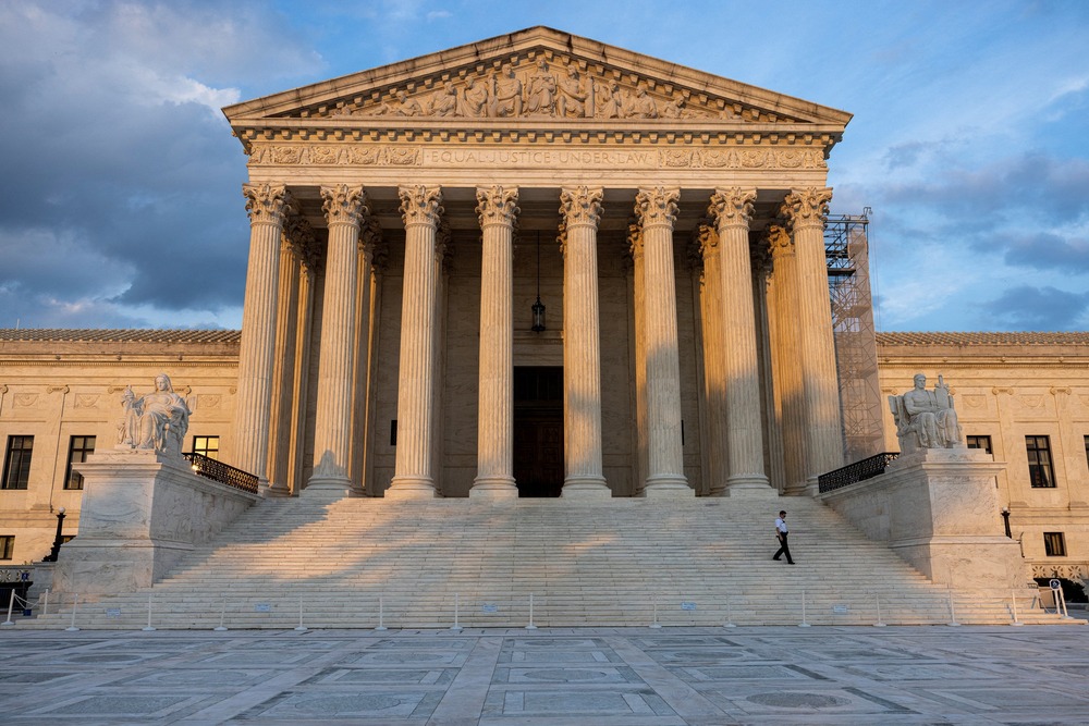 Courthouse looms in the evening light; security guard, dwarfed by building, walks down the stairs. 