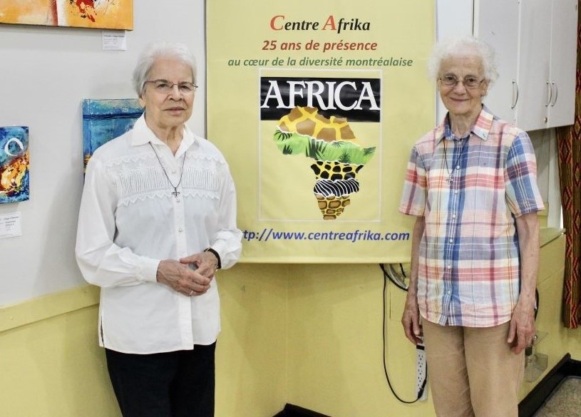 Srs. Monique Bonnefoy, left, and Rita Toutant stand near a sign that reads "25 years at the heart of Montreal's diversity" at Centre Afrika. 