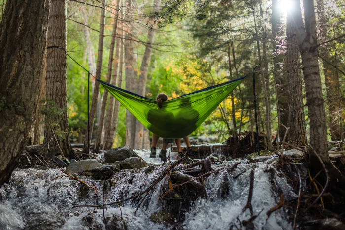 A couple sits in a hammock above a forest stream. (Unsplash/Spring Fed Images)