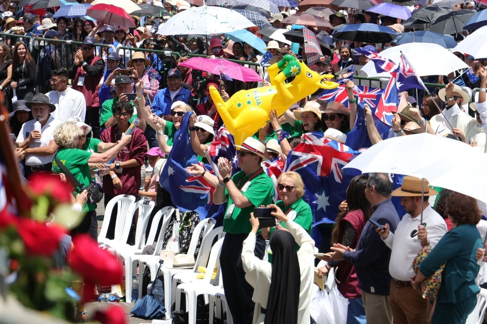 Many people stand from plastic chairs cheering and waving flags etc.