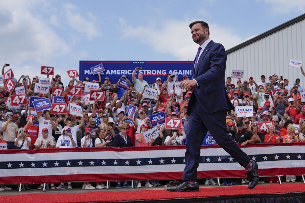 Vance walks across red-carpeted platform; in background, supporters in stands hold signs.