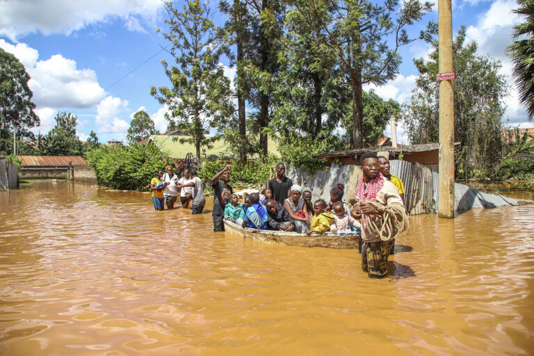 People on boat, and others wading through flooded street. 