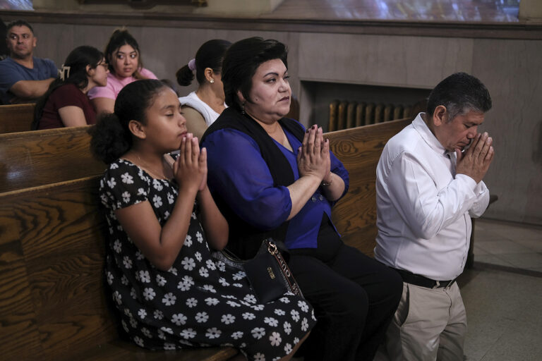 Woman, man, and young girl pray in front pew of church.