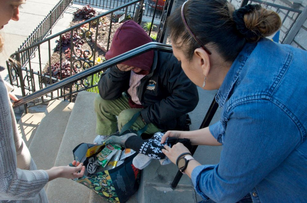 Olivia Sharkey and a staffer offer warm gloves and a hat to a neighbor suffering from the cold March air. iladelphia's Kensington neighborhood. (GSR photo/Dan Stockman) 