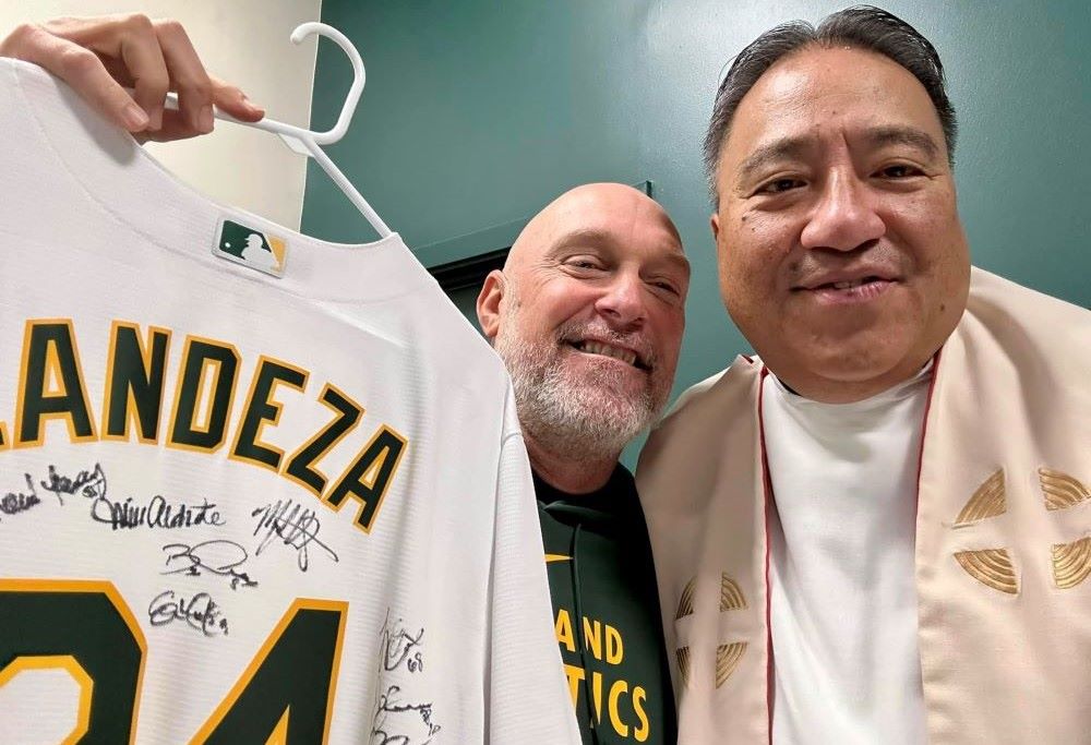 Fr. Jayson Landeza receives a personalized Oakland A's jersey, signed by the players, from the team's manager, Mark Kotsay.