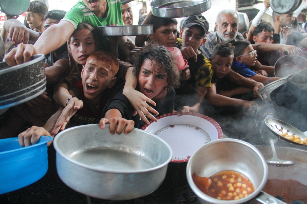 Children holding bowls and pots, their faces marred by deep anguish, clamor one over the other for the food.